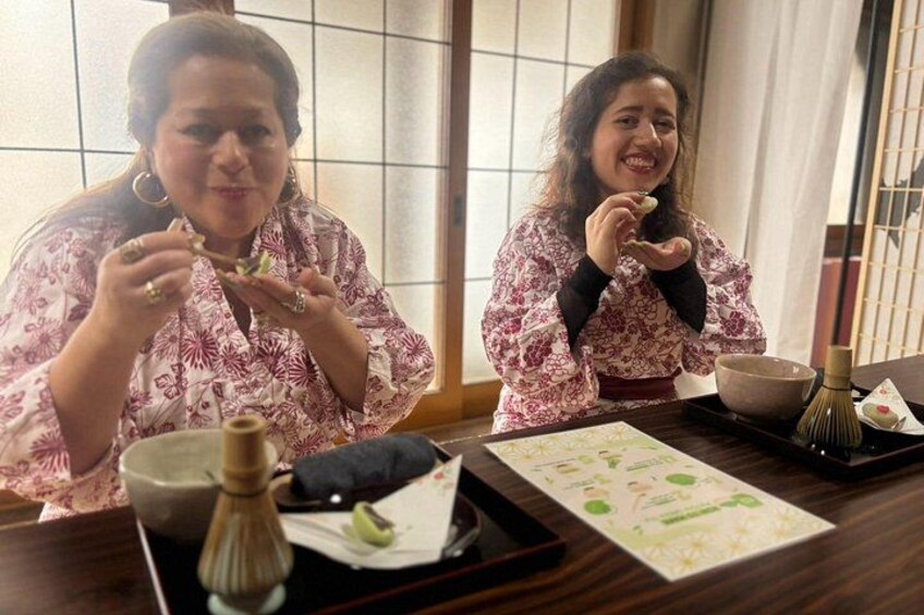 Two people sitting at a table with chopsticks, bowls, and a whisk. 3