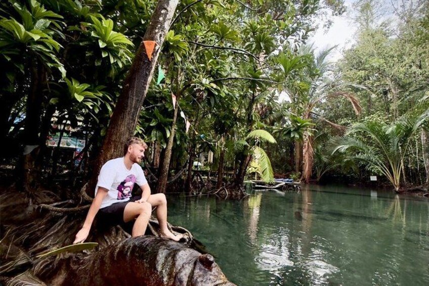 Een persoon zit op een tak aan een rivier, omringd door weelderige vegetatie. 4