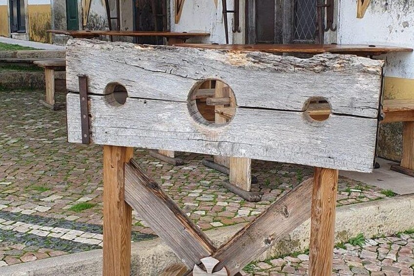 A rustic wooden structure with circular cutouts, possibly a historical artifact or tool, set on a cobblestone surface. 3
