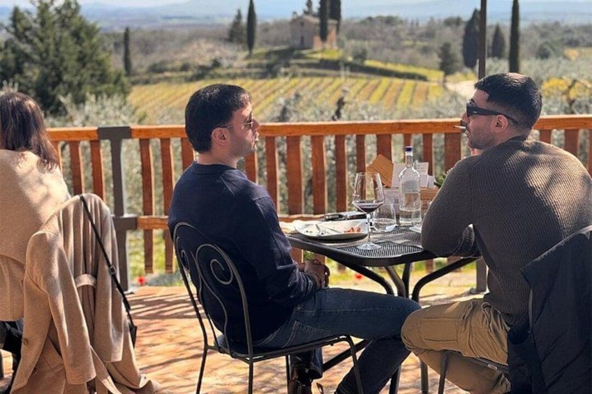 Ein Mann und eine Frau sitzen draußen an einem Tisch, im Hintergrund ein Weinberg. 2