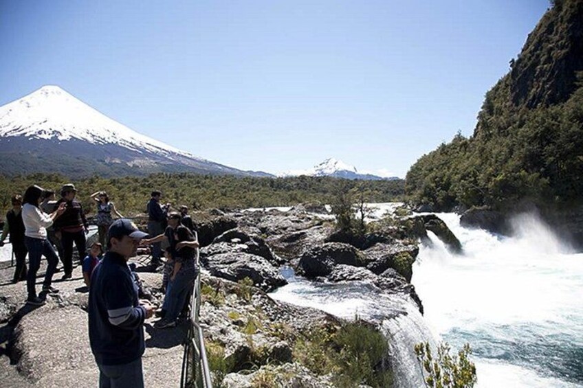 A waterfall, a rocky riverbank, and a snow-capped mountain in the background. 1