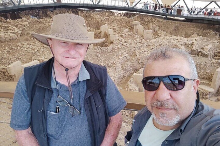 Two people standing in front of an archaeological site with exposed ruins. 2