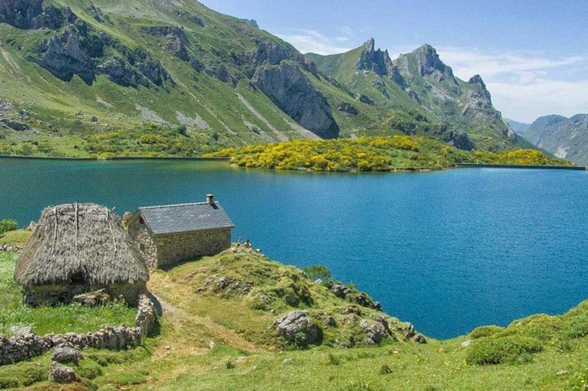 Un lago rodeado de montañas, una cabaña con techo de paja y un edificio de piedra. 1