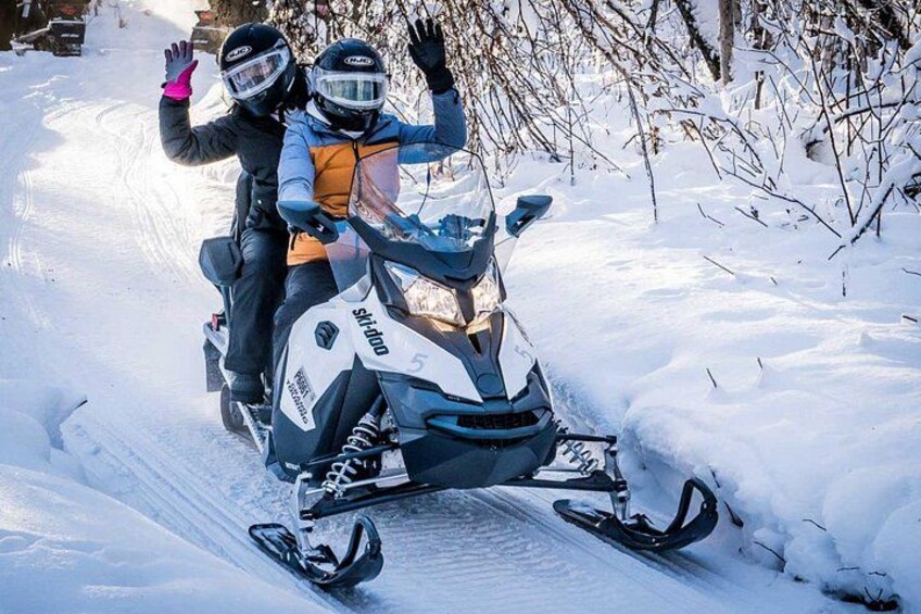 Ein Schneemobil mit zwei Personen, umgeben von schnee bedeckten Bäumen. 5