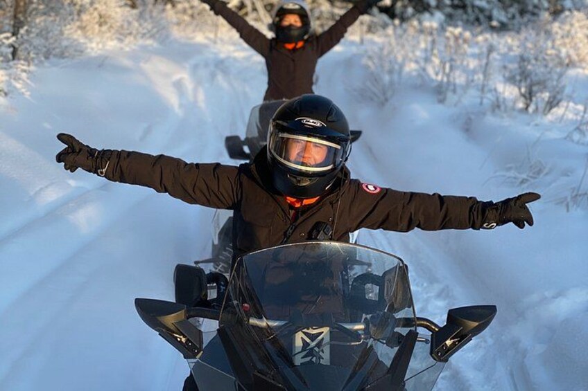 Eine Person auf einem Schneemobil mit ausgestreckten Armen, mit Helm und Jacke bekleidet. 3