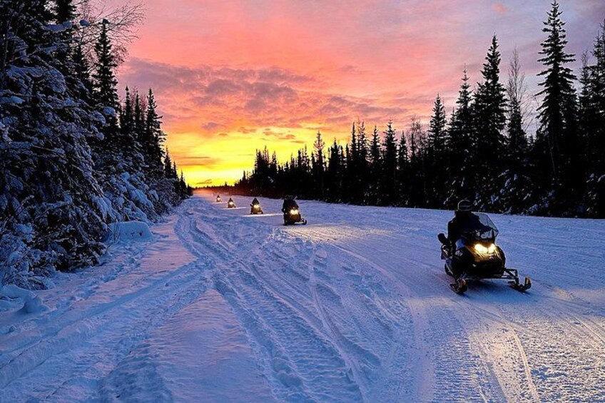 Eine Schneemobilstrecke mit verschneiten Bäumen und einem Sonnenuntergang im Hintergrund. 4