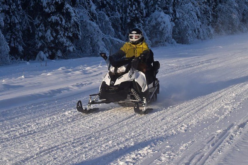 Eine Person fährt mit einem Schneemobil auf einem verschneiten Pfad, im Hintergrund sind Bäume zu sehen. 2