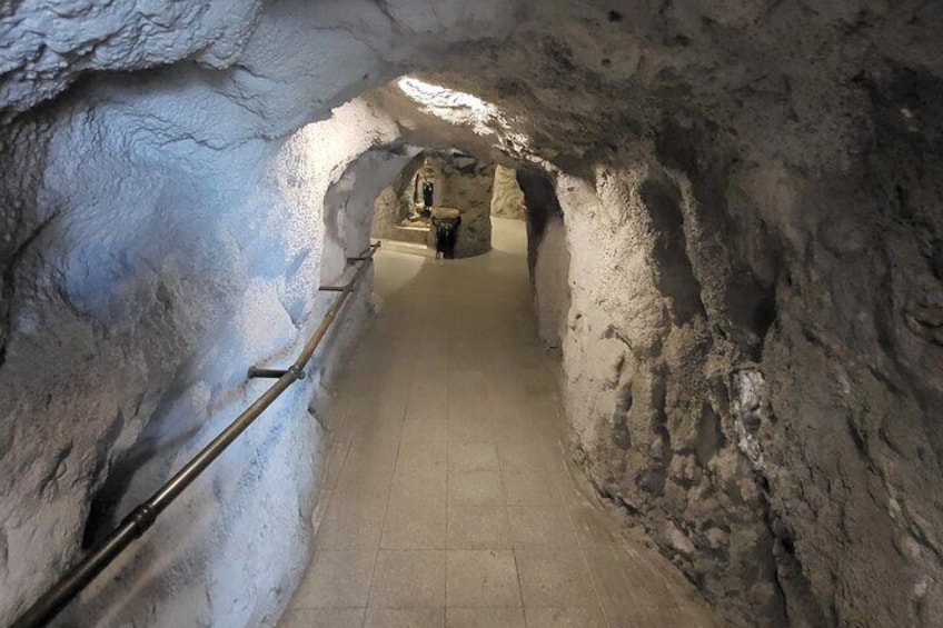 En smal, svagt upplyst tunnel med grova, ojämna väggar och en trästege på vänster sida. 1