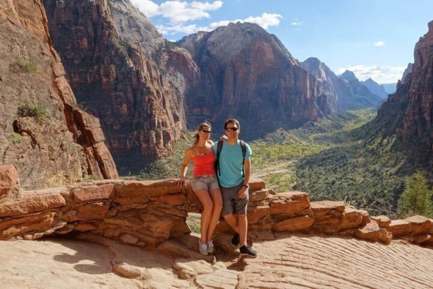Two people standing on a rocky outcrop with a canyon in the background. 1