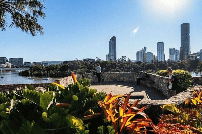 A waterfront park with greenery, a stone wall, and a city skyline in the background. 5