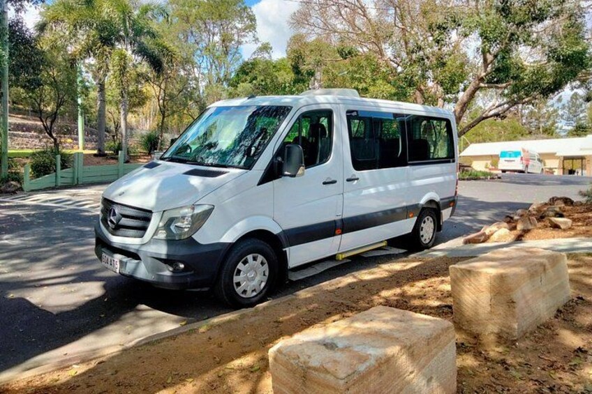 A white van parked on a dirt road with trees and a building in the background. 2