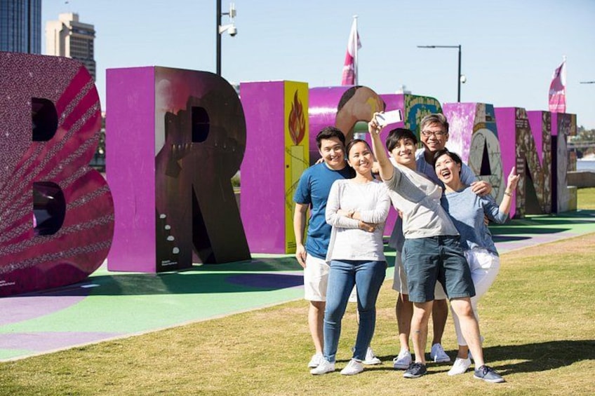 A group of people standing in front of large, colorful letters spelling 'BRITAIN' with a grassy field and a cityscape in the background. 4