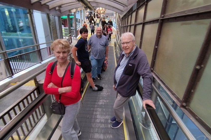 People on an escalator in a modern building with glass railings and metal beams. 3