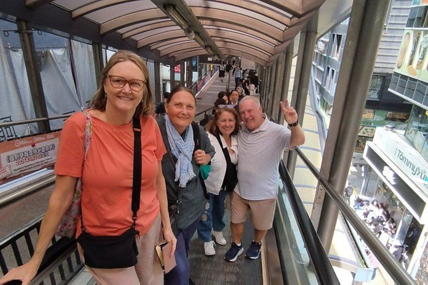A group of people on an indoor escalator with a glass enclosure, surrounded by a modern architectural structure. 4