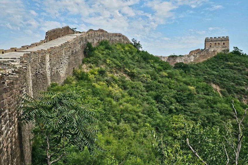 A historical stone wall with a watchtower, surrounded by dense green foliage. 2