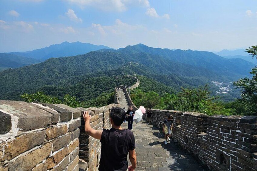 Een persoon staat op de Chinese Muur, met een bergachtig landschap op de achtergrond. 3