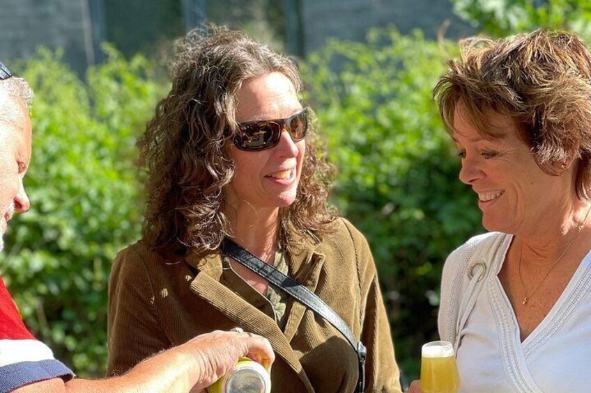 Two people outdoors, one holding a camera and the other holding a drink. 2