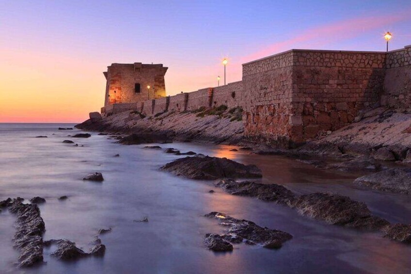 A coastal stone wall with a tower at sunset. 1
