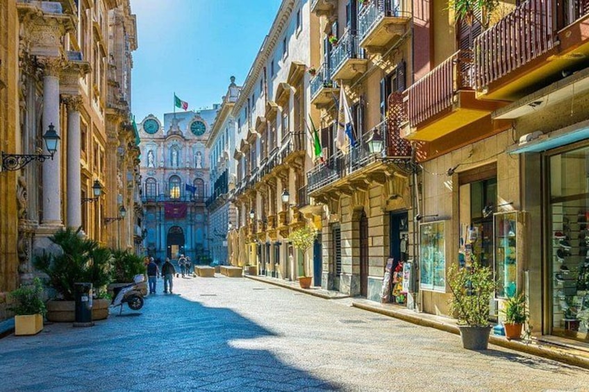 Una strada acciottolata fiancheggiata da edifici storici, una fontana e persone che passeggiano. 1