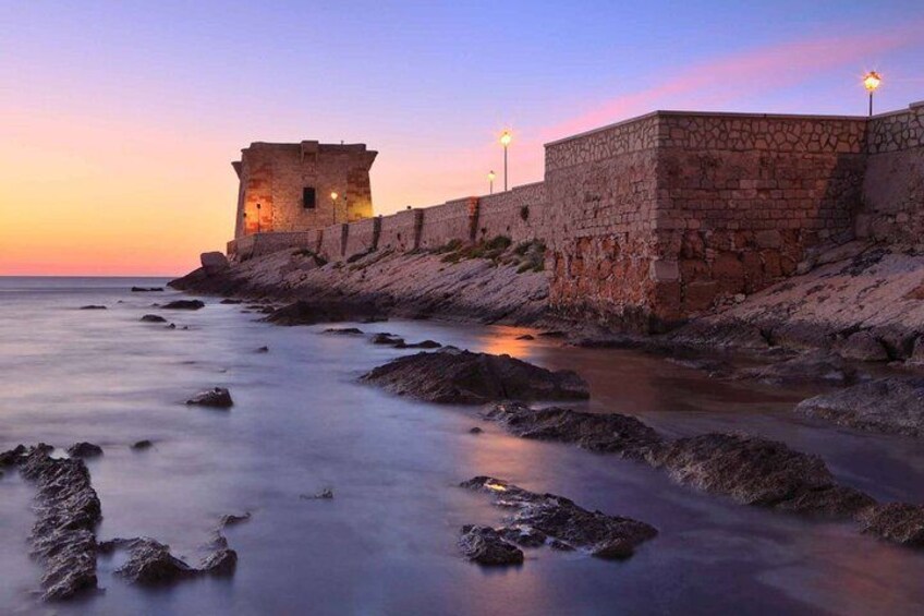 Un muro de piedra frente al mar, una torre, un mar tranquilo y un cielo al atardecer. 2