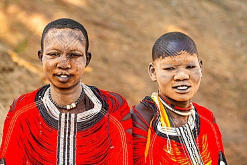 Two individuals in traditional attire with intricate beadwork and a patterned fabric. 1