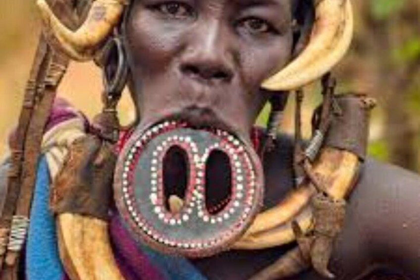 A person wearing a large, ornate necklace with circular elements and a patterned garment. 4