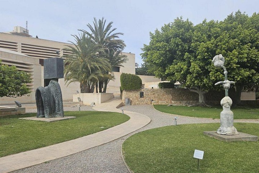 A landscaped garden with a winding path, a stone sculpture, and a palm tree. 4