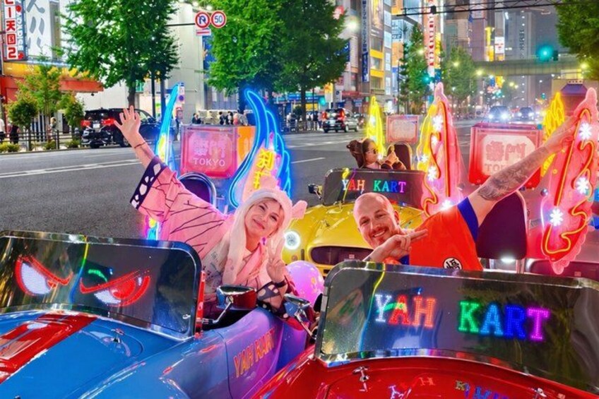 A brightly lit, neon-lit vehicle with 'YAH KART' written on it, parked on a city street at night. 1