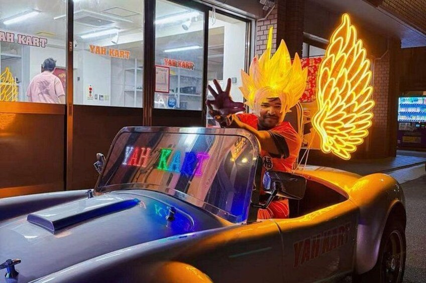 A person in a yellow car with a neon wing decoration, parked in front of a store with a sign that reads 'YAH KART'. 5