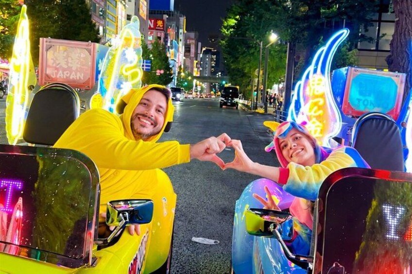 Two people in yellow costumes on a street with neon signs and a 'JAPAN' sign in the background. 2