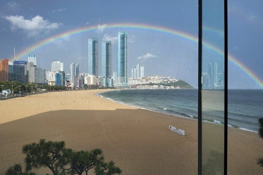 Una playa con un horizonte urbano, un arcoíris y un letrero. 3