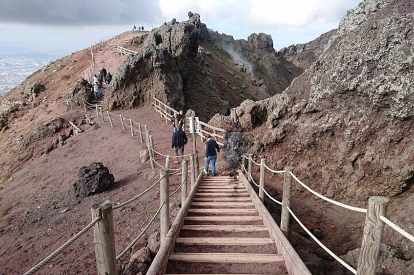Eine Holztreppe führt einen steinigen Hügel hinauf, Menschen steigen hoch. 1