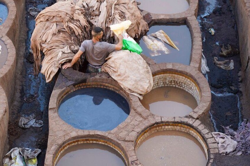 A person sorting materials in a traditional dyeing setup with multiple circular basins. 2
