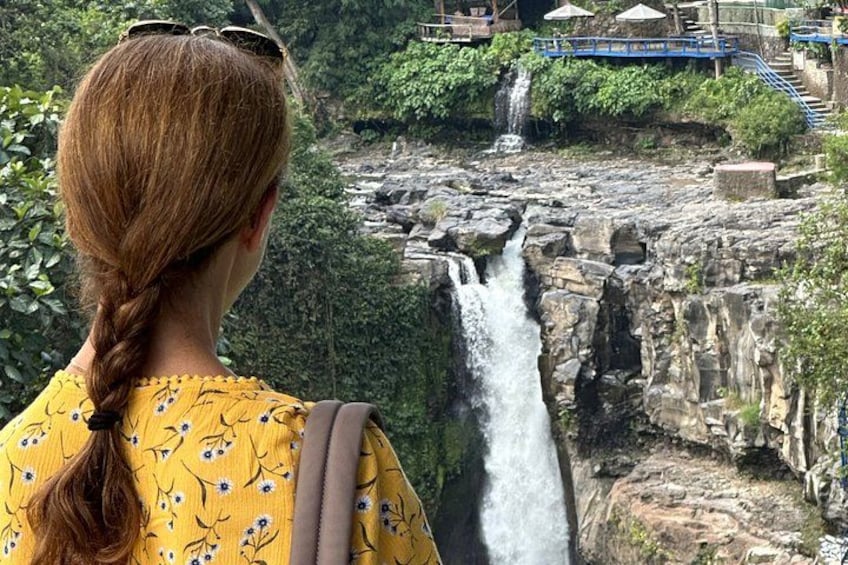 A waterfall cascading down a rocky cliff with a bridge and pathway in the background. 3
