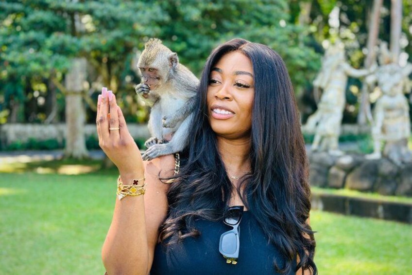 A person holding a monkey in a park with statues in the background. 4