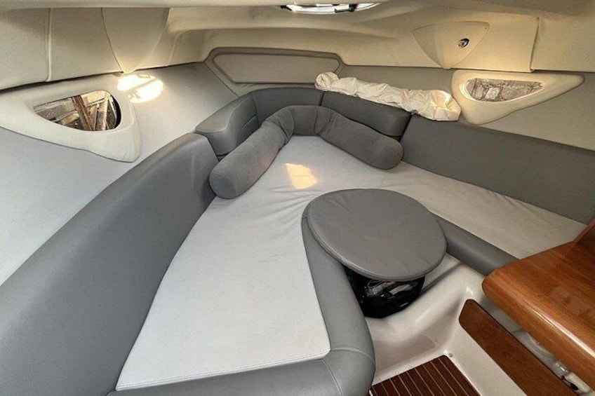 A boat interior with a gray cushioned seating area, a small round table, and a white cover. 4