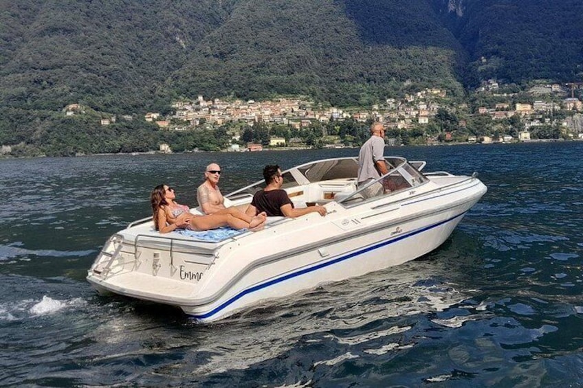 A boat with people on it, water, and a mountainous landscape with buildings in the background. 3
