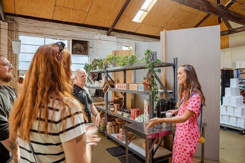 A person in a pink dress standing at a counter with shelves of products and plants in a workshop. 5