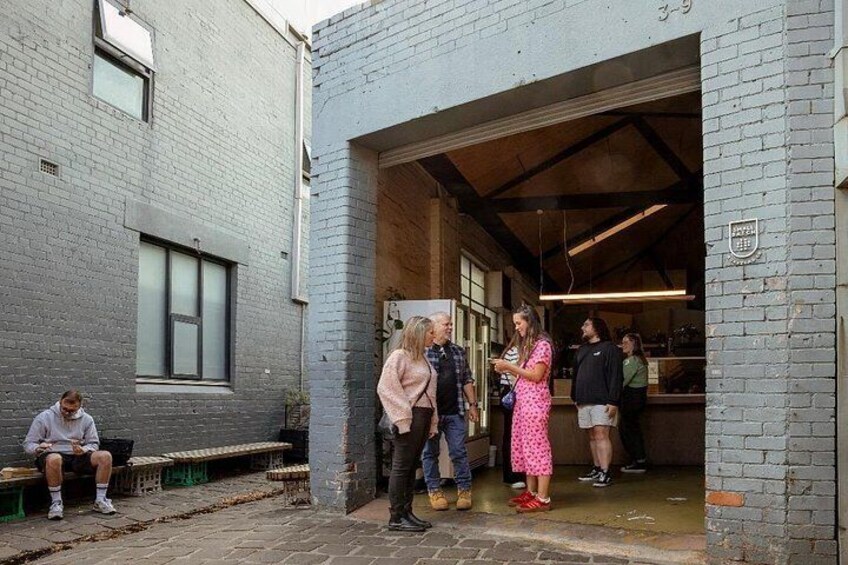A group of people standing outside a building with a brick facade and a large open door. 4