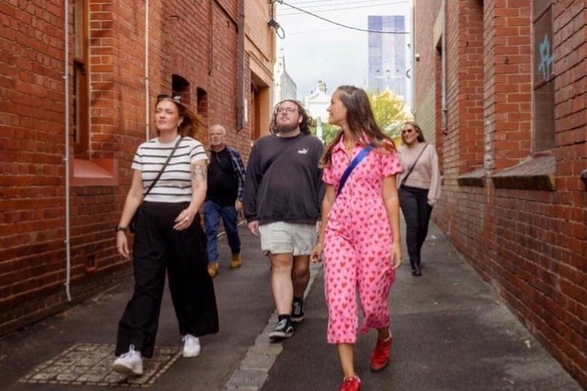 A narrow alley with brick walls, a group of people walking, and a building with graffiti in the background. 1