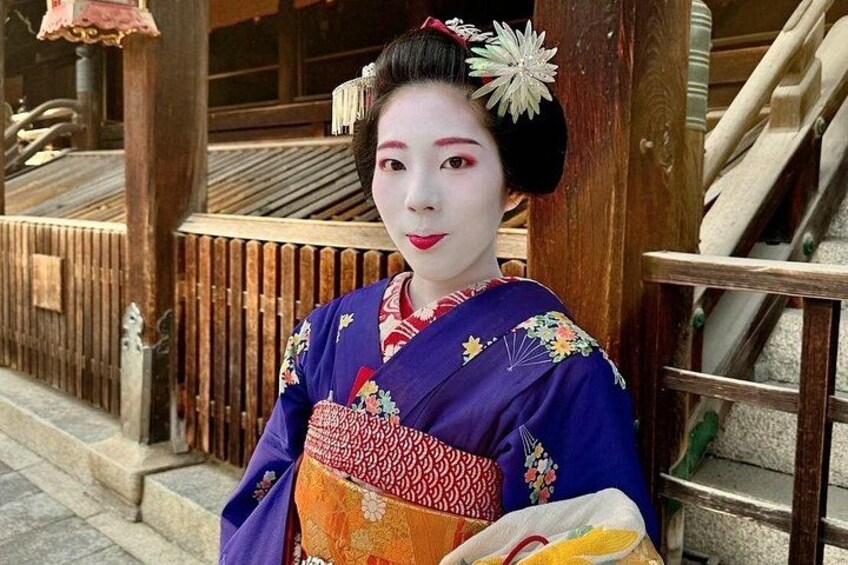 Una persona vestida con traje tradicional japonés, con una estructura de madera y escaleras al fondo. 5