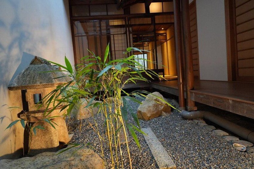 Un jardín japonés tradicional con un farol de piedra, plantas de bambú y un edificio de madera. 2