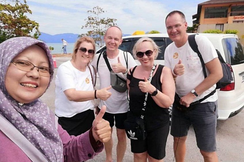 A group of people giving thumbs up near a body of water with mountains in the background. 1