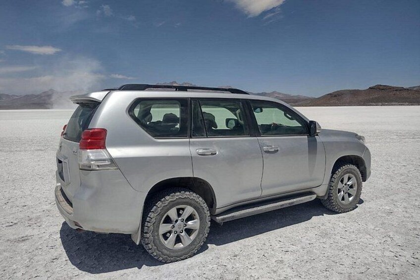 A silver SUV parked on a salt flat with a clear sky. 2