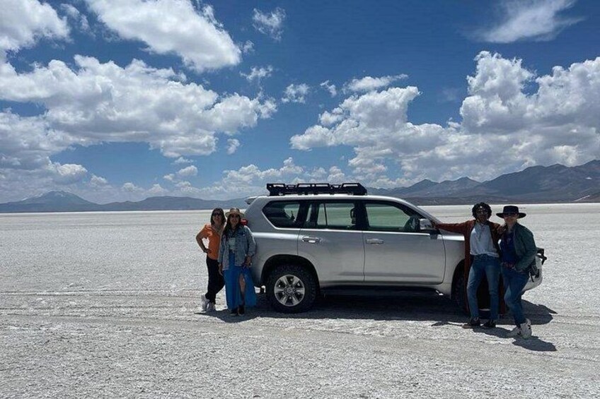 A silver SUV parked on a salt flat with mountains in the background. 3