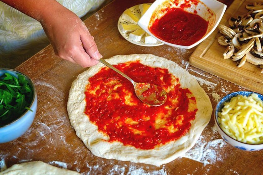 A person preparing pizza dough with tomato sauce and cheese on a wooden table. 1
