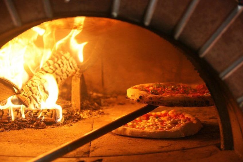 A wood-fired pizza oven with flames and two pizzas inside. 4