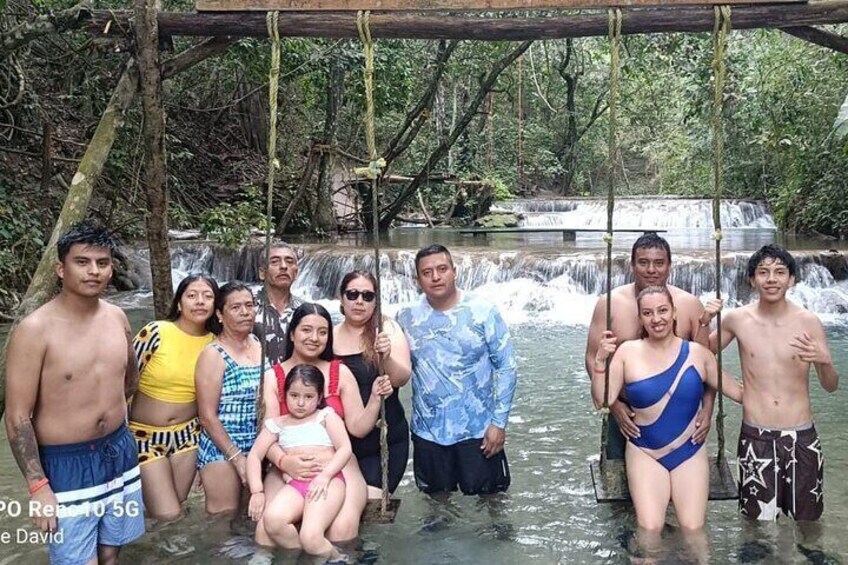 A group of people posing in front of a waterfall in a forested area. 5