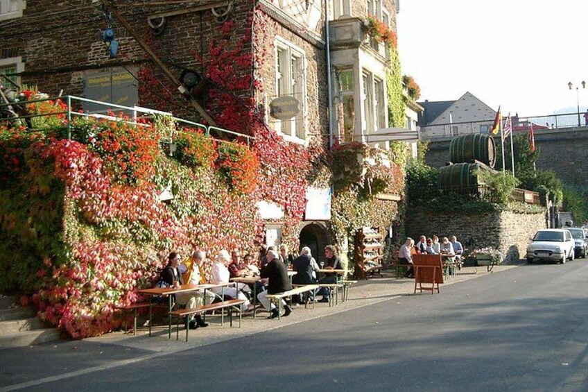 A street with outdoor seating, a building with ivy, and a stone wall. 3