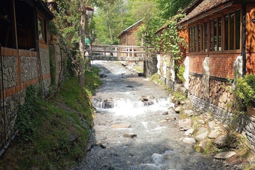 Un arroyo serpentea por un pueblo rústico de muros de piedra y construcciones de madera. 2